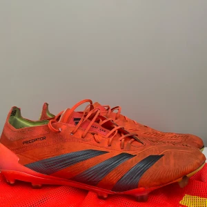 Adidas Predator fotbollsskor orange - Ett par slitna Addidas preditor med påse Säljer ett par Adidas Predator fotbollsskor i en riktigt fet orange färg med svarta detaljer och gula sulor. Skorna har snörning och är designade för gräsplan, med coola Predator-loggor undertill. Perfekta för dig som vill sticka ut på planen.