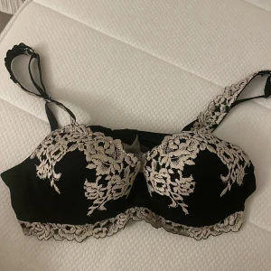 Svart BH med spetsdetaljer - Supersnygg svart BH med ljusa spetsdetaljer och blommigt mönster över kuporna och axelbanden.  Köp ifrån Intimissimi 
