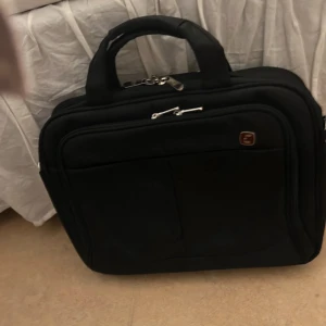 Svart datorväska med flera fack - Säljer en svart datorväska från Swissgear med flera praktiska fack och robusta handtag. Väskan har silverfärgade dragkedjor och en stilren design som passar perfekt för att bära laptop och tillbehör. 