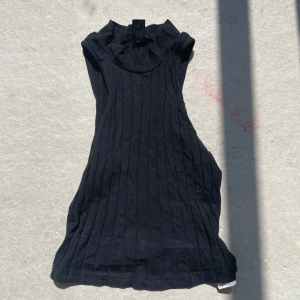 Svart ribbad ärmlös polotopp - Säljer en svart ärmlös polotopp med ribbad struktur och hög krage. Toppen har en tight passform och är tillverkad i ett mjukt stickat material som ger en snygg siluett. Perfekt att styla med jeans eller kjol för en clean look.