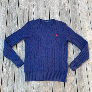 Marinblå kabelstickad tröja Polo Ralph Lauren - Säljer en marinblå kabelstickad tröja från Polo Ralph Lauren med rund halsringning och röd broderad logga på bröstet. Tröjan är i storlek S och personen på bilden är 176. Den är i 100% siden. Det finns inga defekter. Passar perfekt som den är eller som övertröja till en skjorta!Hör av er om frågor!