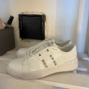 Valentino Rockstud vita sneakers - Snygga vita Valentino Rockstud sneakers i skinn med ikoniska silverfärgade nitar längs sidorna och på tungan. Klassisk rund tå, platt sula och snörning framtill. 
