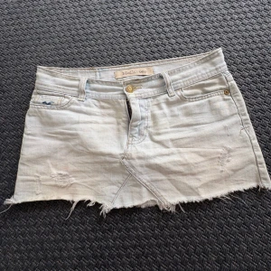 Ljus jeanskjol från Hollister - Snygg ljusblå jeanskjol från Hollister med rå kant och slitna detaljer. Klassisk femficksmodell med dragkedja och knapp framtill.  Midjemått: ca 36 cm  och hela längden från midjan längst ner: ca 24 cm🥰