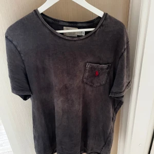 t-shirt från Polo Ralph Lauren - Snygg grå/svart t-shirt från Polo Ralph Lauren med klassisk passform. T-shirten har en bröstficka med röd broderad logga och rund halsringning. Perfekt basic-plagg med stilren vibe. Sjukt snygg tvätt, str L , skick 8/10! Pris 299 