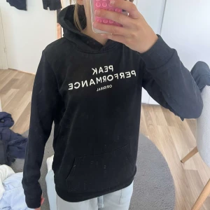 Svart hoodie från Peak Performance - Svart hoodie från Peak Performance med vit logga framtill och liten vit detalj på ärmen. Magficka och huva på tröjan. Skön passform och passar till allt. Priset går att diskuteras!🥰