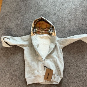 Grå Burberry hoodie med dragkedja - Snygg grå hoodie från Burberry med klassiskt rutigt foder i huvan. Helt oanvänd för att storleken passade ej. Den är M men passar egentligen perfekt XS/S. Pris kan diskuteras 