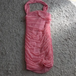 Rosa kortklänning - Supersöt rosa kortklänning med omlott-detaljer och draperad effekt. Klänningen har breda axelband och är tillverkad i ett lätt, syntetiskt material som ger en snygg struktur. Perfekt för dig som vill sticka ut med en feminin och trendig look.