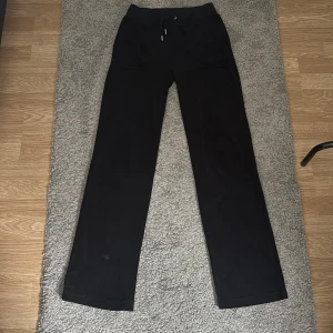 Svarta mjukisbyxor med snörning - Svarta mjukisbyxor med raka ben och dragsko i midjan. Byxorna har två fickor fram och två bakfickor med lock och silverfärgade knappar. Mjukt material och relaxed vibe, perfekt för chill dagar. Säljer pga att min syster ej använder dem och har knappt gjort det!