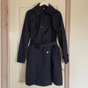 Trenchcoat från Armani Jeans - Jättefin marinblå trenchcoat från Armani Jeans med klassisk design. Storlek EU48, motsvarar M/L.  Jackan har långa ärmar, knappar och ett bälte i midjan för en stilren look. Perfekt för både vår och höst. Mycket bra skick, inga fläckar eller andra defekter. 