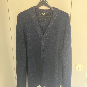 Mörkblå kofta med knappar - Säljer en stilren mörkblå kofta från Arket med knappar framtill. Koftan har en v-ringad design och långa ärmar, perfekt för kyligare dagar. Den är tillverkad i ett mjukt material som ger en bekväm passform. Perfekt för att lägga till en touch av elegans till din garderob. Oversized då jag själv oftast har XL.