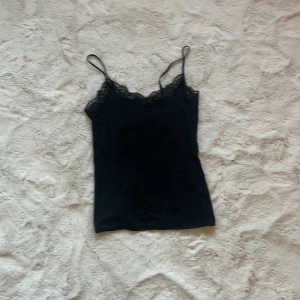 Svart linne med spetsdetaljer - Snyggt svart linne med smala axelband och vacker spetskant vid urringningen. Perfekt för en stilren look.