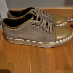 Beige sneakers med bruna detaljer - Snygga sneakers i beige med bruna detaljer och snörning. Skorna har en rund tå och en vit sula som ger en stilren look. Perfekta för en avslappnad stil.