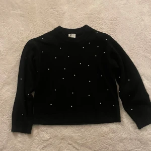 Svart tröja med pärlor - Säljer en elegant svart tröja dekorerad med små pärlor. Tröjan har långa ärmar och en klassisk passform. Perfekt för att ge en touch av stil till din garderob.
