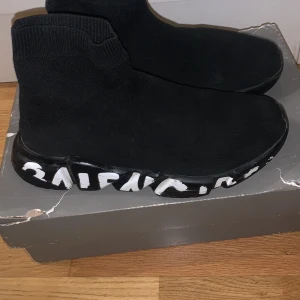 Svarta sneakers från Balenciaga speed runnet - Säljer ett par svarta Balenciaga sneakers med texturstickat material. Skorna har en unik design med vit text på sulan och en strumpliknande passform. Perfekta för dig som vill ha en stilren och modern look. Skorna är äkta och kmr med vestaire collective authentic bekräftelse