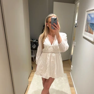 Vit klänning med spetsdetaljer - Säljer en vit klänning med spetsdetaljer och v-ringning från Zara. Den är aldrig använd men har ej lappen kvar.