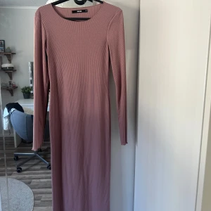 Rosa ribbad klänning från Bik Bok - Säljer en stilren rosa ribbad klänning från Bik Bok. Klänningen har en lång design med långa ärmar och en rund halsringning. Perfekt för en elegant och bekväm look.