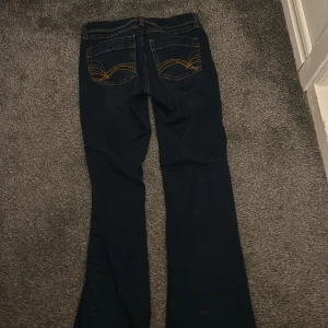 Mörkblå bootcut lågmidjade jeans från H&M Divided - Snygga mörkblå bootcut jeans från H&M Divided. De har en klassisk femficksdesign och dekorativa sömmar på bakfickorna. Perfekta för en stilren look.