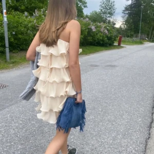 Beige volangklänning - Säljer en söt beige klänning med flera lager av volanger. Klänningen är axelbandslös och har en luftig passform, perfekt för varma dagar. Den är kort och ger en lekfull känsla. Perfekt för sommarens alla tillfällen!