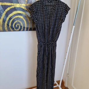 Mönstrad jumpsuit med knytband - Snygg jumpsuit i svart med vita fyrkantiga mönster. Den har korta ärmar och ett knytband i midjan för en justerbar passform. Perfekt för en stilren look.