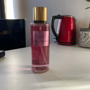 Pure Seduction Body Mist från Victoria's Secret - Säljer en fräsch och fruktig body mist från Victoria's Secret, Pure Seduction. Flaskan är rosa med en gyllene kork och rymmer en doft av saftig plommon och krossad fresia. Perfekt för en uppfriskande känsla hela dagen.