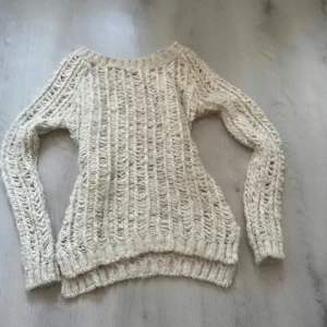Beige stickad tröja - Säljer en mysig beige stickad tröja med ett luftigt mönster. Tröjan har långa ärmar och ribbade kanter vid ärmslut och nederkant. Perfekt för sommardagar och strand besök!