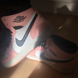 Nike Air Jordans i rosa och svart - Snygga Nike Air Jordans i en fräsch kombination av rosa, svart och vitt. Skorna har den klassiska Air Jordan-loggan på sidan och svart snörning. Perfekta för att ge din outfit en sportig touch.