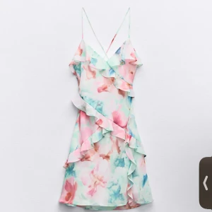 Blommig klänning med volanger - Säljer en färgglad blommig klänning med volanger och smala axelband. Använd 1 gång!