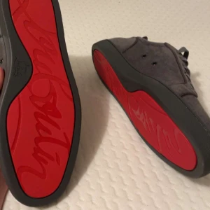 Grå mockasneakers med röd sula - Poppulära grå skor med röd sula. Snygga grå sneakers i mocka med den ikoniska röda sulan. Skorna har snörning och en rund tå, vilket ger en stilren look. Perfekta för dig som vill vara snygg med en unik detalj. Skorna är i storlek 46 men passar mer 44 eller 45. Skorna är aldrig använda utan endast testade. Box ingår tyvärr inte