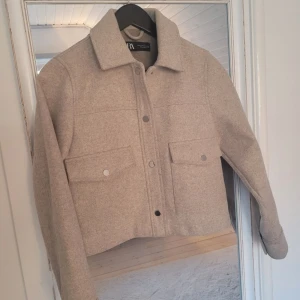 Beige jacka från Zara - Snygg beige jacka från Zara med en croppad design och knappar framtill. Perfekt för en stilren look.