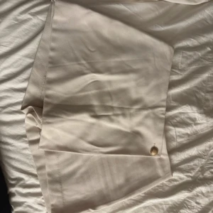 Beige kjol från hm - Säljer en stilren beige kjol från hm med en elegant knappdetalj framtill. Kjolen har en klassisk design och är perfekt för en chic look. Passar bra till både vardag och speciella tillfällen.