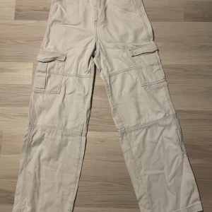 Beige cargobyxor - Säljer ett par beige cargobyxor med flera praktiska fickor på sidorna. Byxorna har en avslappnad passform och är perfekta för en casual look. De är tillverkade i ett slitstarkt material och har en klassisk design.