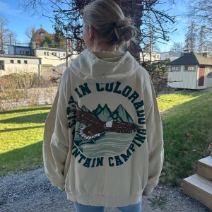 Beige hoodie från pull&bear - Säljer en beige hoodie från pull&bear med texten 'Denver City in Colorado Mountain Camping' tryckt på både fram- och baksidan. Hoodien har en mysig insida och en stor luva. Pris går att diskutera!