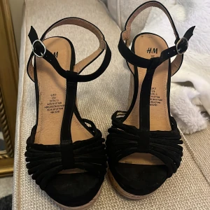 Svarta kilklackssandaler från H&M - Snygga svarta sandaler med kilklack från H&M. De har en öppen tå och justerbara remmar med spänne. Perfekta för sommarens alla tillfällen.
