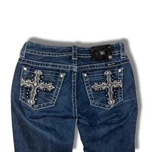 Miss Me Jeans - Snygga mörkblå jeans från Miss Me med unika broderade korsdetaljer. Jeansen är bootcut med kontrasterande sömmar. Inga defekter förutom att några ”nitar” ramlat av och att en liten del av M ramlat av, se bild 4, 5. Men märks inte ifall man inte kollar noggrant. Står storlek 26 men är ganska liten i storleken. [Midjemått: 33cm] [Innerbenslängd: 81cm] Skriv om du har några funderingar! 