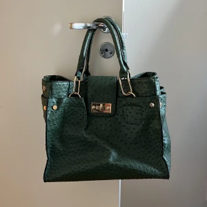 Grön handväska med struktur - Skit snygg grön handväska med en unik strukturerad yta och guldfärgade detaljer. Väskan har två handtag och en stängning framtill. Insidan är rymlig med flera fack för enkel organisering. 💞