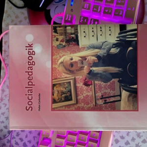 Socialpedagogik - Boken 'Socialpedagogik' av Helen Carlander, utgiven av Sanoma Utbildning, är en omfattande guide inom ämnet socialpedagogik. Den har ett rosa omslag med ett foto på framsidan. Perfekt för studenter och yrkesverksamma inom socialt arbete.