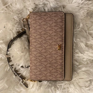 Beige axelväska från Michael Kors - Snygg axelväska från Michael Kors i beige med ett diskret mönster. Väskan har en justerbar axelrem och flera fack inuti för kort och andra småsaker. Perfekt för att hålla ordning på dina grejer med stil. Använd 2 gånger så kommer i mycket fint skick!