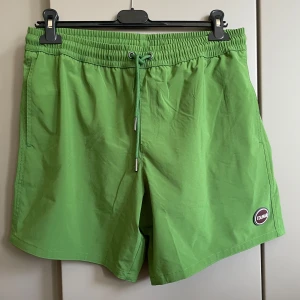 Gröna bad shorts från italienska Colmar - Snygga gröna shorts från Colmar med elastisk midja och snörning för perfekt passform. De har en bakficka med lock och ett diskret märke på framsidan. Perfekta för sommarens alla äventyr!