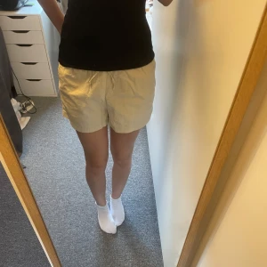 Beige bomullsshorts - Säljer ett par bekväma beige shorts i bomull. De har en elastisk midja för en skön passform och är perfekta för varma dagar. Shortsen har en enkel design utan mönster eller extra detaljer.