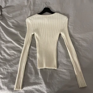 Vit ribbad långärmad topp - Säljer en stilren vit ribbad topp med långa ärmar. Perfekt för lager-på-lager eller som den är. Enkel och elegant design som passar till många tillfällen.