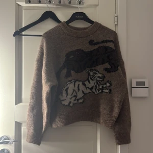 Beige stickad tröja med djurmotiv från Carin Wester - Säljer en beige stickad tröja från Carin Wester med ett coolt djurmotiv i svart och vitt. Tröjan har en rund hals och långa ärmar, perfekt för att hålla sig varm och stilren. Passar perfekt för höst och vinter!