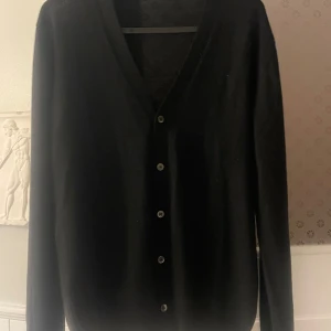 Svart kofta från Gran Sasso - Elegant svart kofta från Gran Sasso, tillverkad i Italien. Den har en v-ringad design med knappar framtill och är gjord av jungfru ull för extra komfort. 