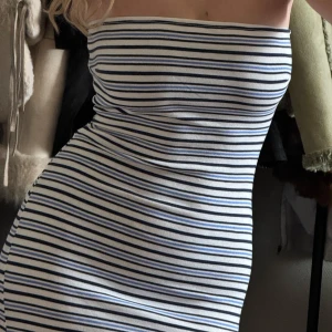 Randig klänning med smala axelband - Säljer en stilren randig klänning med smala axelband. Klänningen har ett mönster av svarta och blå ränder på vit bakgrund. Den är figurnära och perfekt för en somrig look.