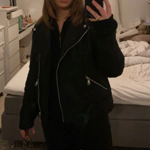 Svart skinnjacka med dragkedja - Säljer en snygg svart skinnjacka med dragkedja och silverfärgade detaljer. Jackan har en klassisk bikerstil med långa ärmar och en asymmetrisk dragkedja framtill. Perfekt för en cool och edgy look!