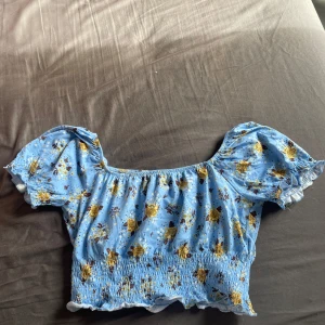 Blå blommig offshoulder topp - Charmig blå offshoulder topp med blommigt mönster i gult och brunt. Perfekt för varma sommardagar! Knappt använd
