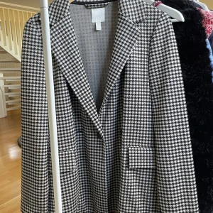 Rutig kavaj från H&M - Snygg rutig kavaj från H&M i svart och vit. Kavajen har en klassisk krage och långa ärmar, perfekt för en stilren look. Passar bra till både vardag och mer uppklädda tillfällen. Storlek 34 ❤️