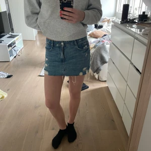 Jeanskjol från Zara - Säljer en cool jeanskjol från Zara med slitna detaljer och rå kant. Kjolen har en klassisk fyrficksdesign och är perfekt för en avslappnad look. Den är kort och har en snygg blå tvätt. Perfekt för dig som vill ha en trendig stil! 💙