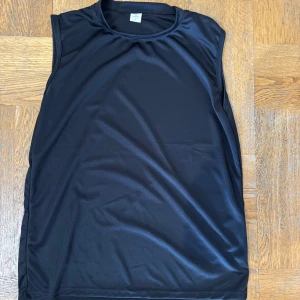 Svart ärmlös topp - Säljer en stilren svart ärmlös topp i ett mjukt och följsamt material. Perfekt för gym och träning eller som ett basplagg i garderoben. Storlek L, och har 10 styckna så ju flera man köper desto billigare. 