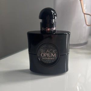 Black Opium parfym från Yves Saint Laurent - Säljer en parfym  av Black Opium från Yves Saint Laurent. Flaskan är svart med en glittrande detalj i mitten och har en rundad kork. Perfekt för den som älskar en djärv och sensuell doft. Parfymen är aldrig använd då den inte är min typ av parfym