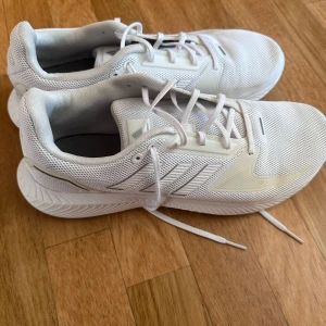 Vita sneakers från Adidas - Snygga vita sneakers från Adidas med klassisk design och snörning. Skorna har en rund tå och är tillverkade i syntetmaterial med en bekväm sula. Perfekta för en stilren look.